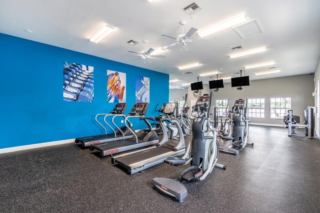 fitness center with cardio training equipment. Tvs hanging from the ceiling. Gym photos on the wall.