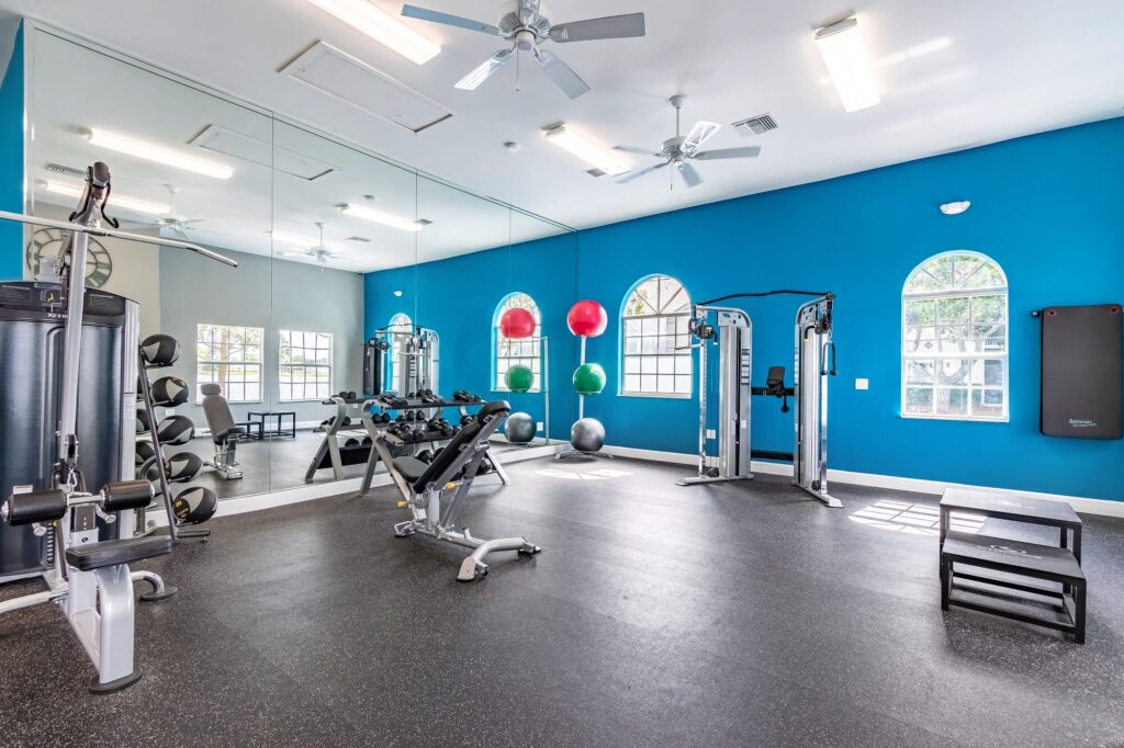 fitness center with strength training equipment with wall of mirrors and ceiling fans