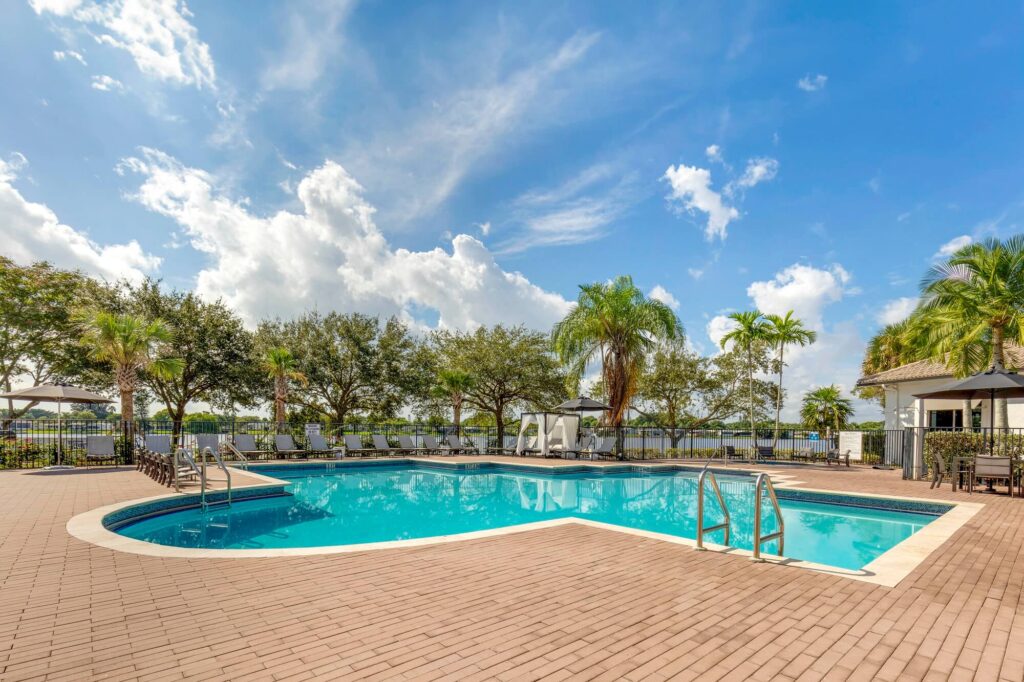Gated pool area with lounge chairs in the back and tables with umbrella and chairs
